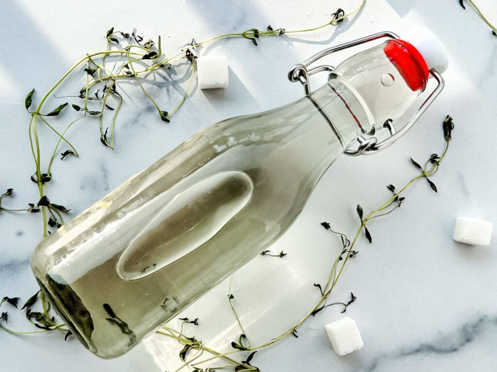 Photo of thyme simple syrup in a glass jar surrounded by thyme sprigs