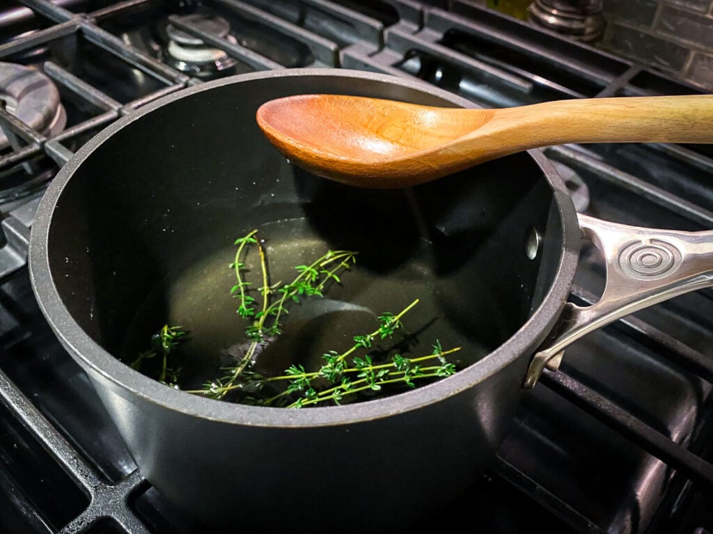 Photo of fresh thyme sprigs in a sauce pan of simple syrup steeping