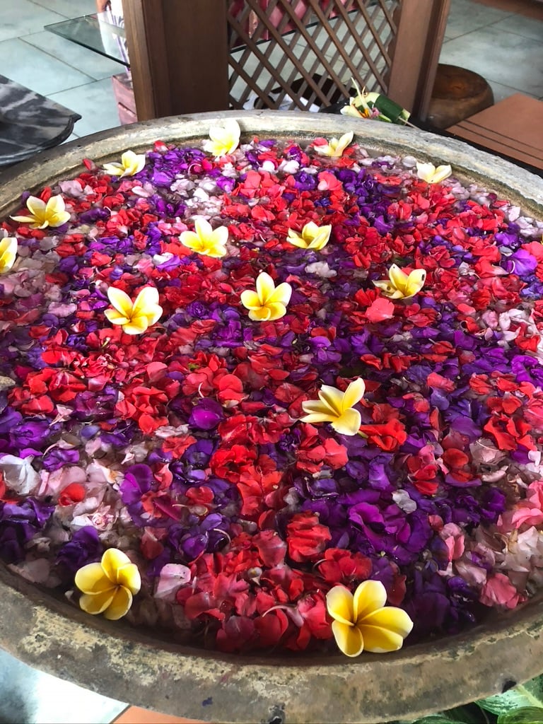 photo of a stone sink filled with red, purple, and yellow flowers inside the  Bebek Bengil restaurant in Ubud Bali