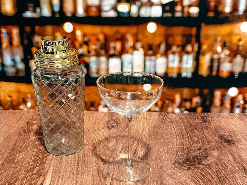 Photo of rimmed coupe glass with cinnamon and sugar and a cocktail shaker