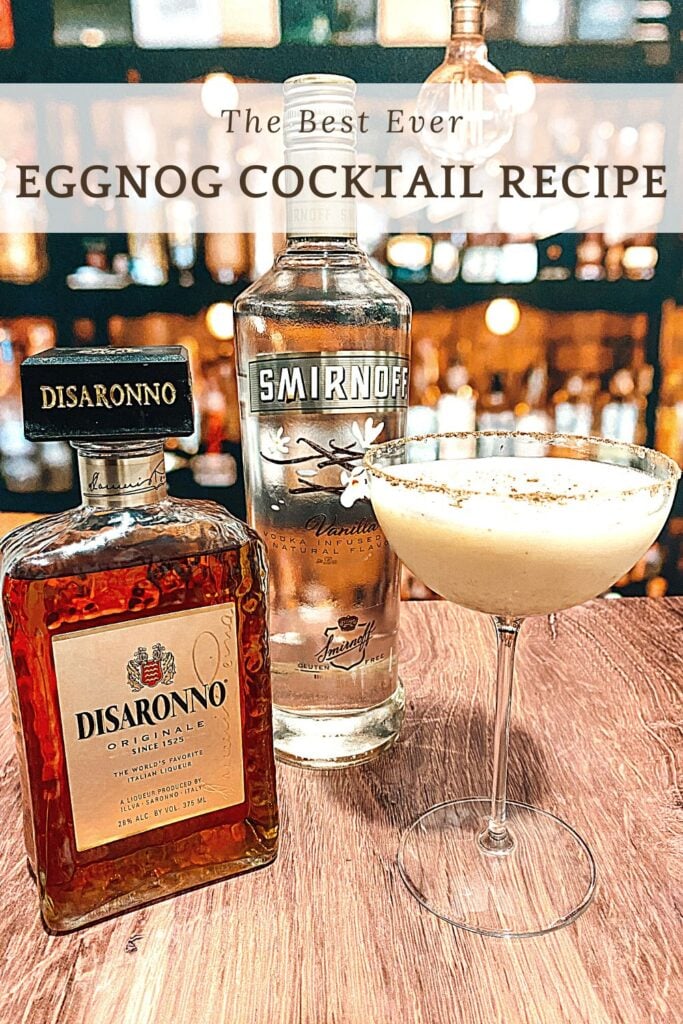 Photo of spiked eggnog in coupe glass wit a bottle of vodka and disaronno