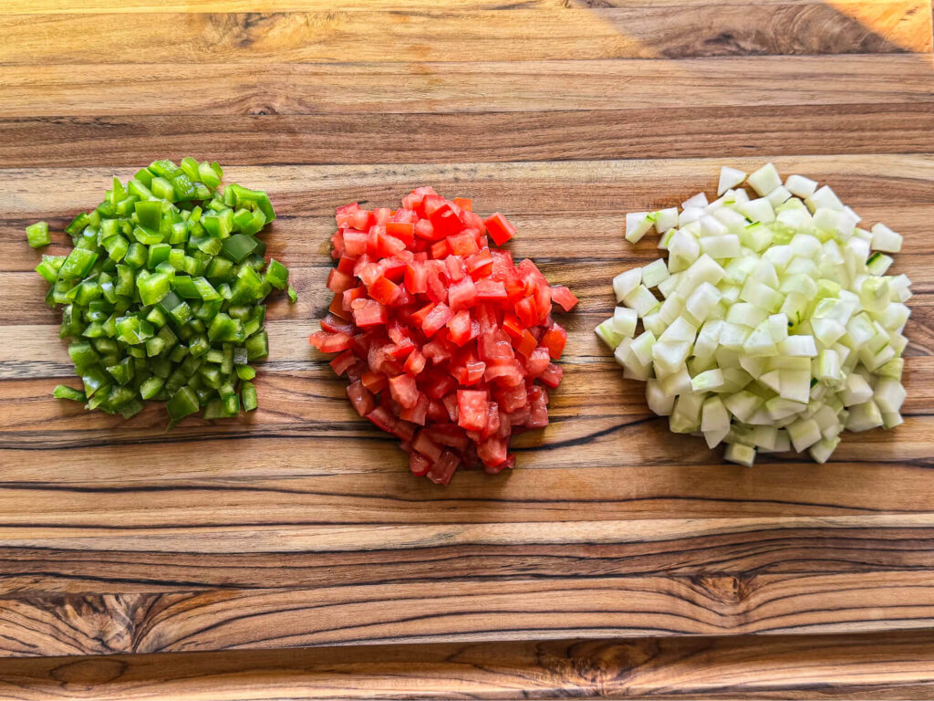 photo of chopped bell peppers, tomatoes, and cucumbers on a wooden cutting board