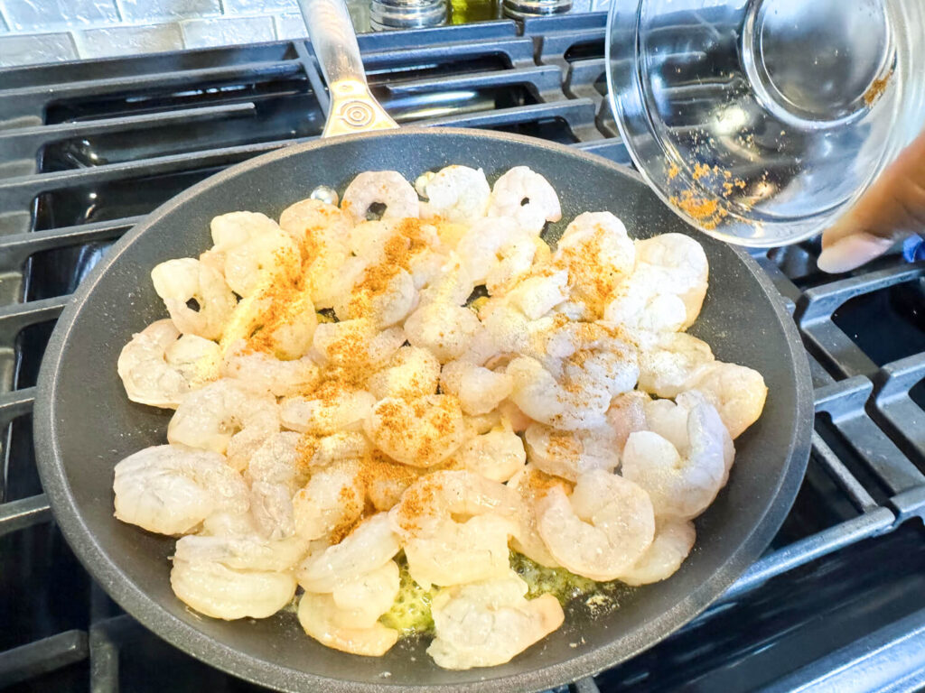 photo of old bay seasoning being added to shrimp in a pan