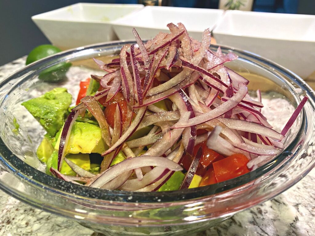 Close up of avocados, red onions and cherry tomatoes in mixing bowl