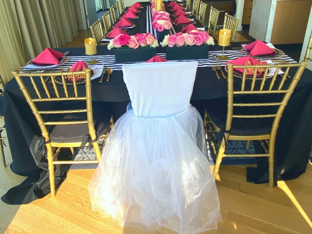 Photo of bridal shower table that's pink, black, white and gold with custom bride chair cover