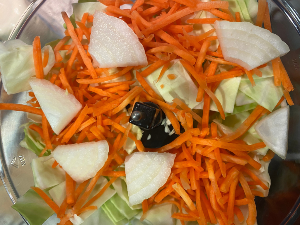 Photo of onions, shredded carrots, and cabbage in a food processor