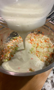 Photo of coleslaw dressing being poured over chopped cabbage and carrots.