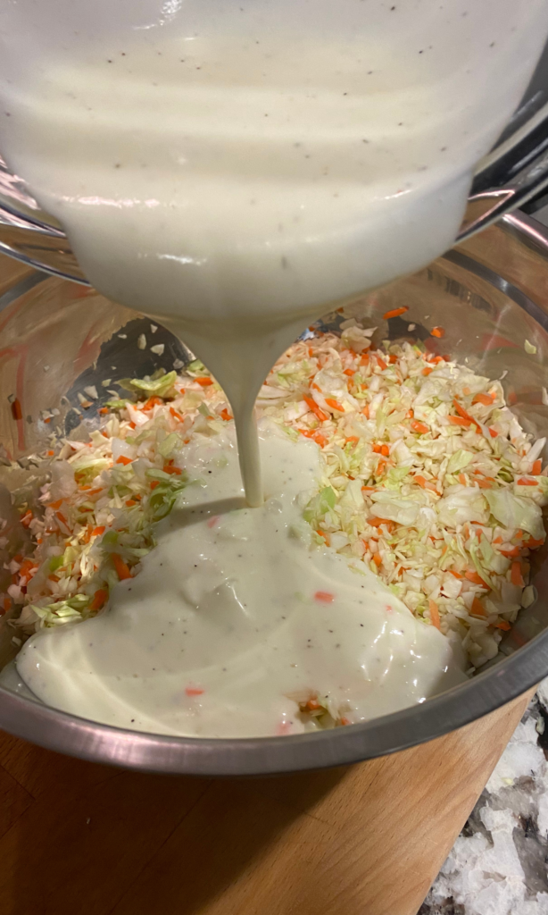 Photo of coleslaw dressing being poured over chopped cabbage and carrots.