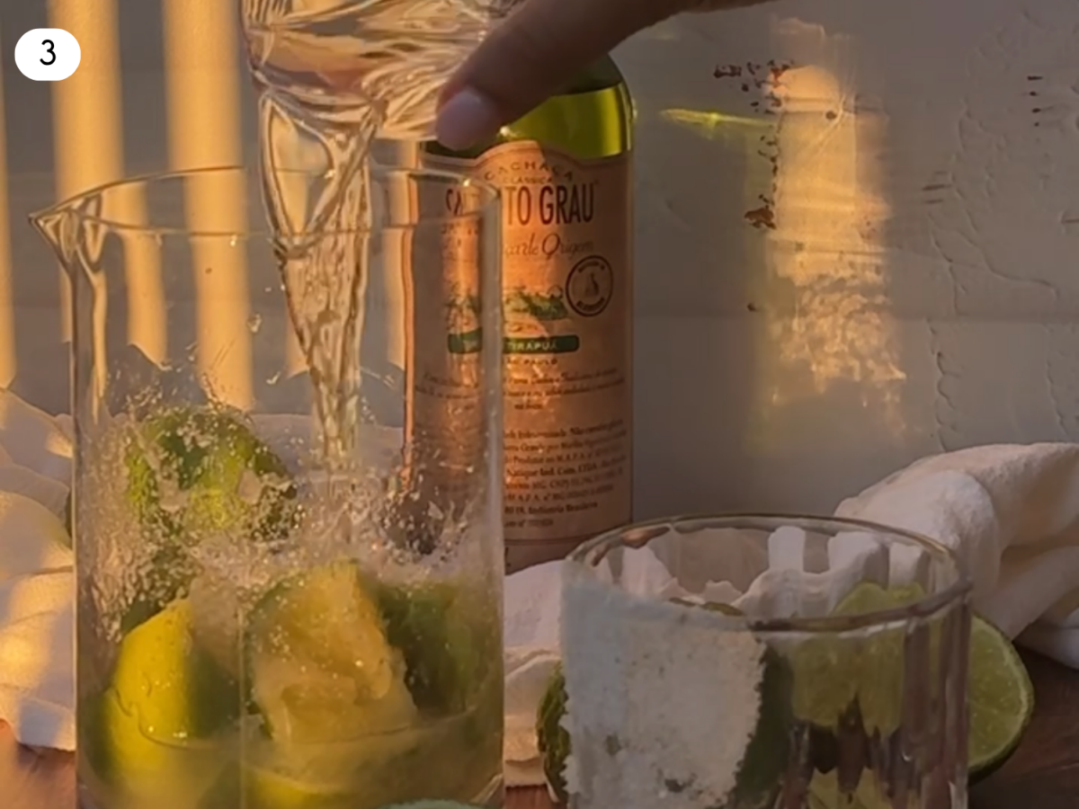 step 3 photo showing Cachaça being poured into the mixing glass with limes and sugar