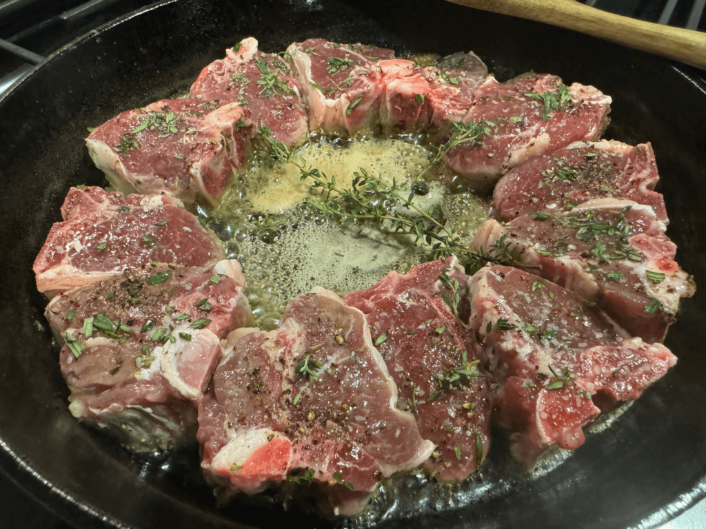 photo of lamb chops cooking in a cast iron pan with butter and herbs