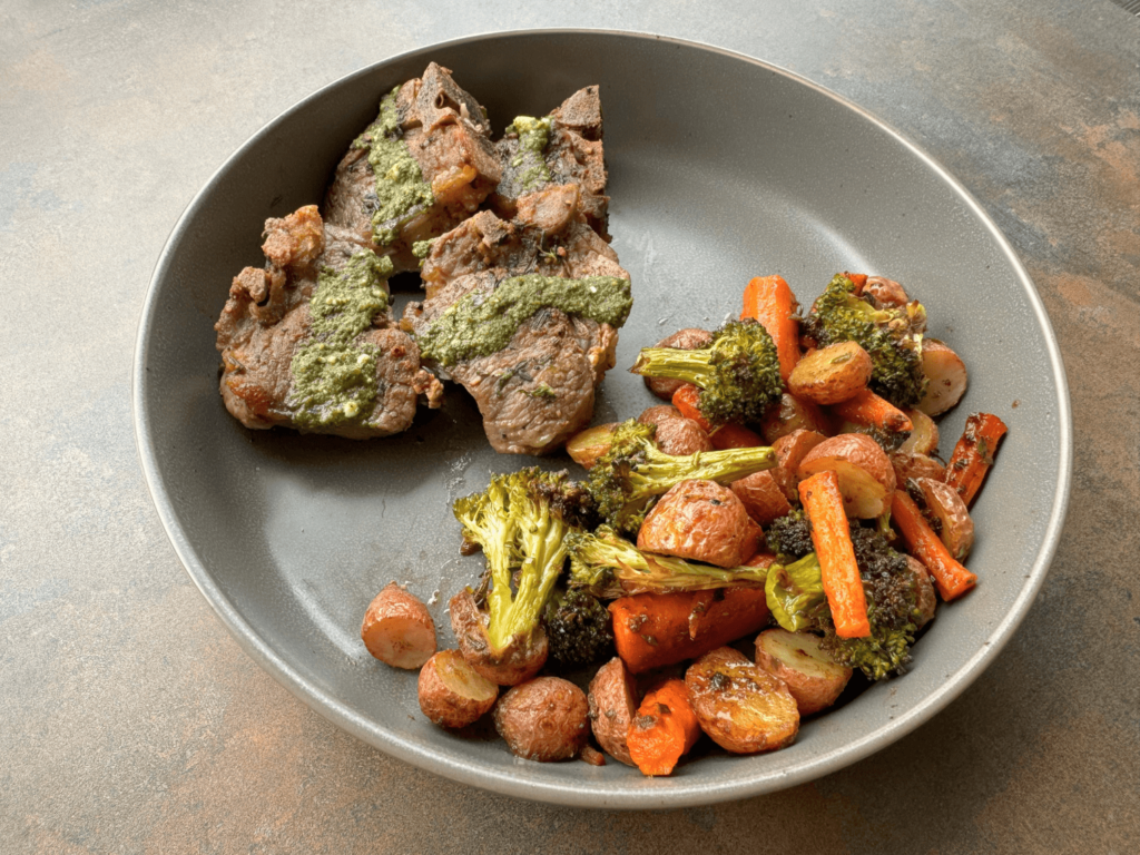 Photo of pan seared lamb with a mint pesto sauce on top with oven roasted carrots, broccoli, and baby red potatoes