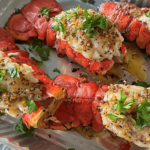 Up close photo of grilled lobster tails in a metal pan with a parsley garnish