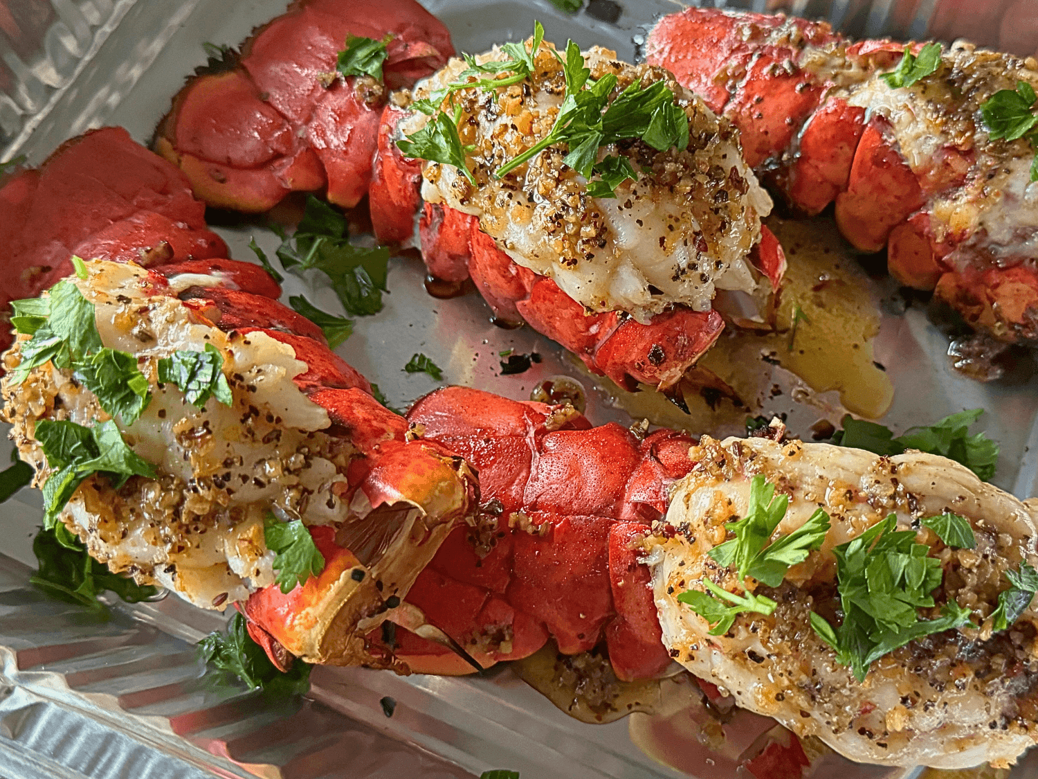 Up close photo of grilled lobster tails in a metal pan with a parsley garnish