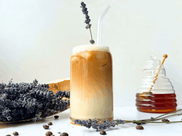 Photo of an iced lavender latte next to a honey jar and a bouquet of lavender flower buds