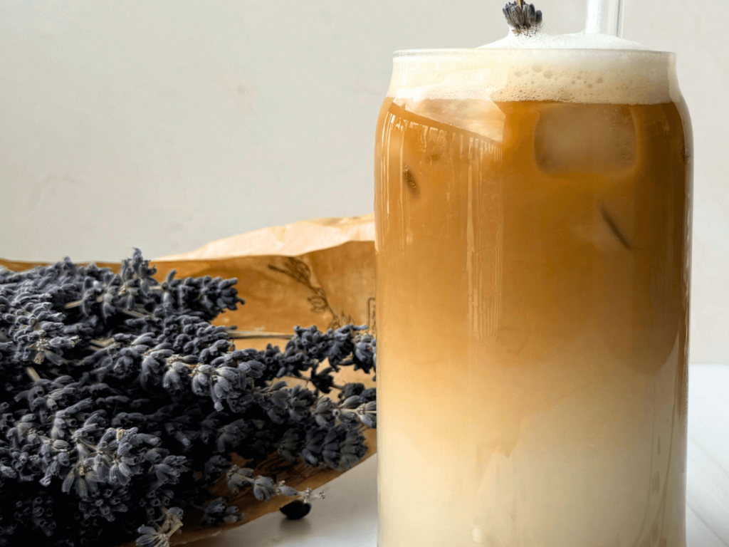 Photo of an iced lavender latte next to a honey jar and a bouquet of lavender flower buds