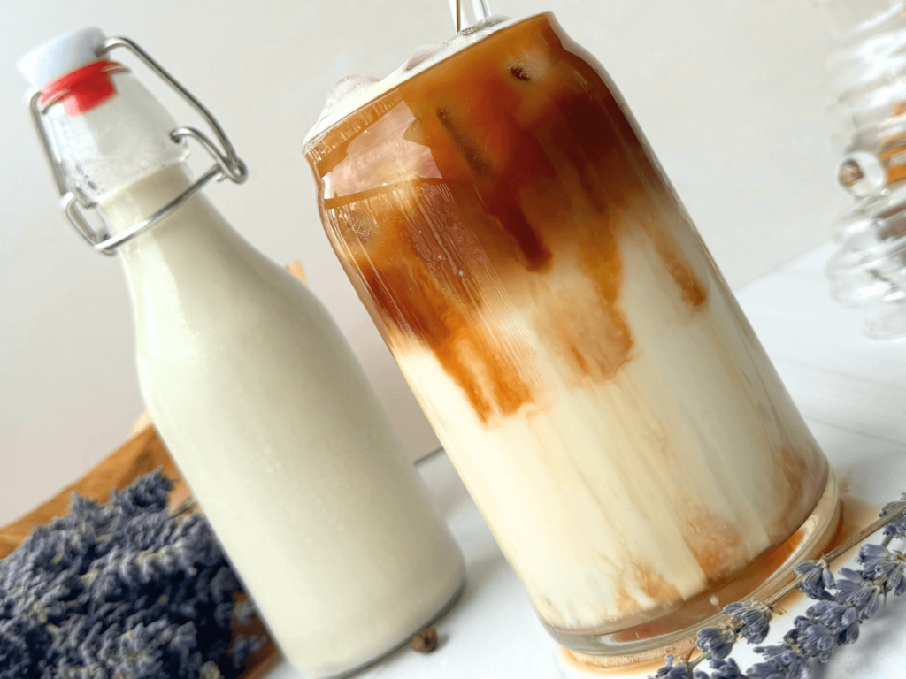 Photo of an iced lavender latte next to a milk jar and a bouquet of lavender flower buds
