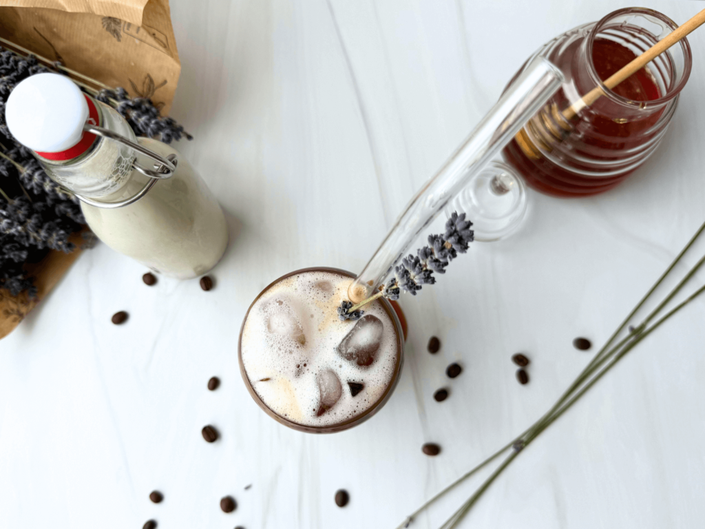 Photo of an iced lavender latte next to a honey jar and a bouquet of lavender flower buds