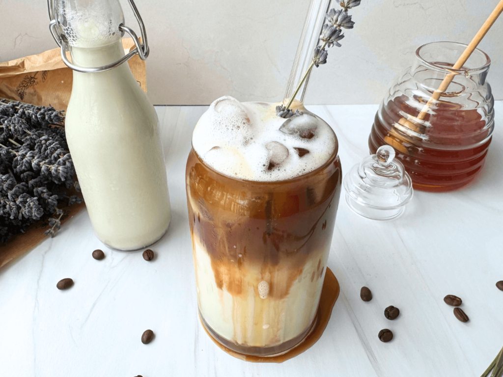Photo of an iced lavender latte next to a honey jar and a bouquet of lavender flower buds
