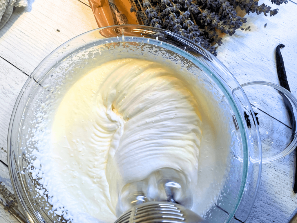 close up photo of hand mixer in a bowl of heavy cream that is whipped