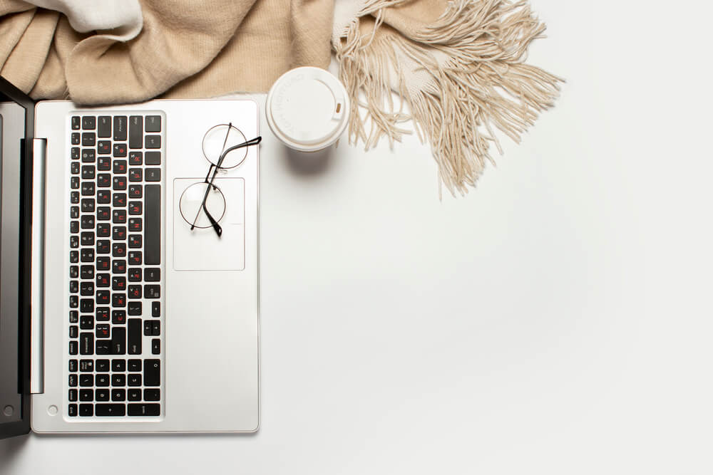 photo of a laptop, classes, and a blanket on a soft tan color surface.