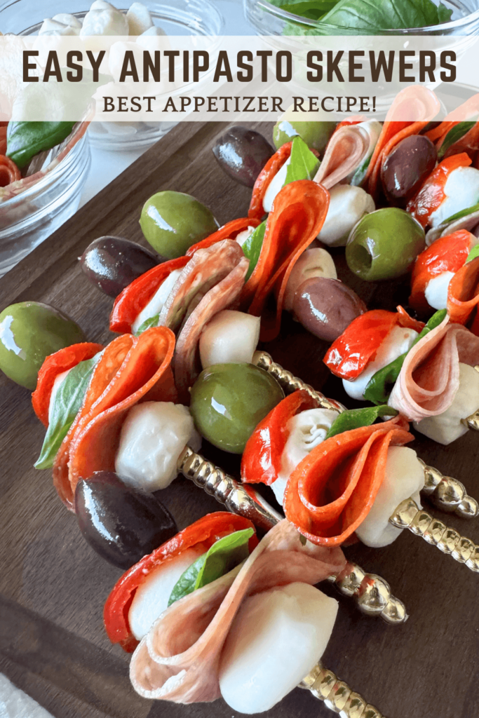 up close photo of antipasto skewers on a wooden cutting board with olives, pepperoni, mozzarella, sweet hot peppers, salami, and basil on a gold fork