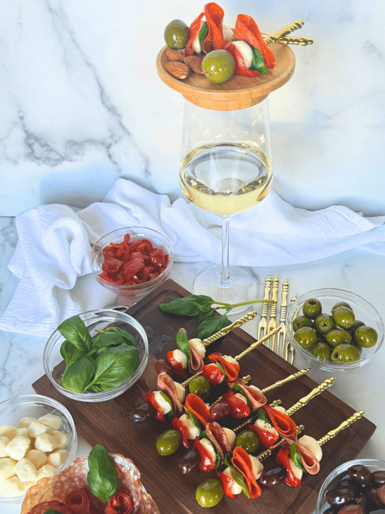 anitpasto skewers on top of a wine galss with a board full of antipasto skewers as well