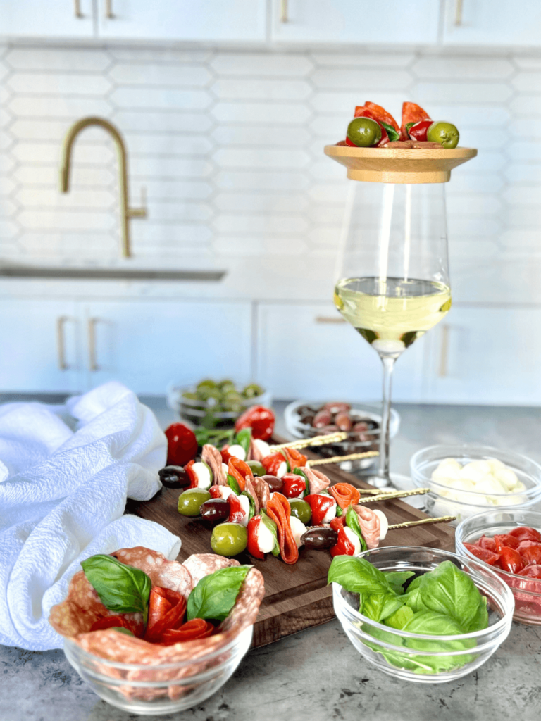 anitpasto skewers on top of a wine galss with a board full of antipasto skewers as well