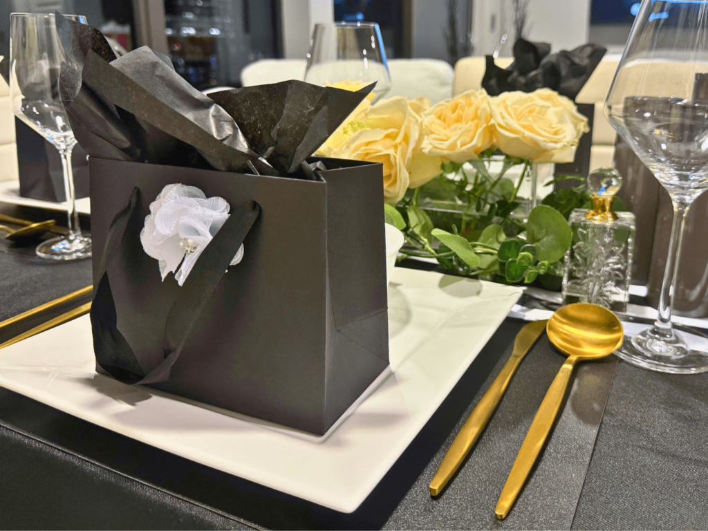 photo of perfume party gift favor in a black bag on a dinner plate with a white flower in the middle