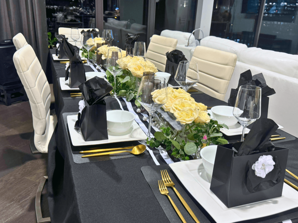 close up photo of the perfume party tablescape. Black linen, white plates, gold forks and spoons, and gifts on top of the white plates