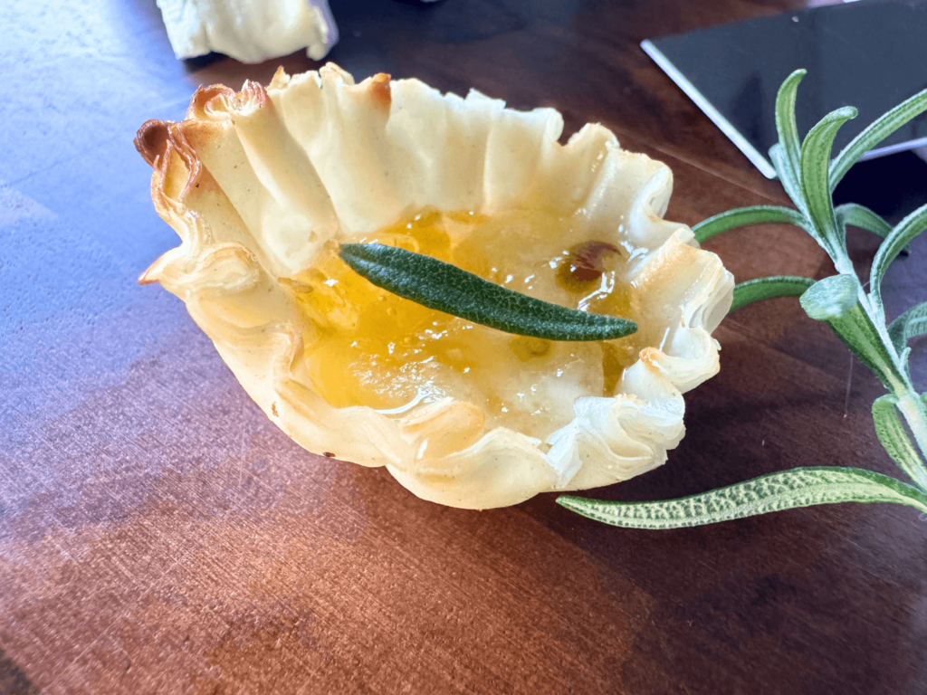 close up photo of one mini baked brie bite with a rosemary on top