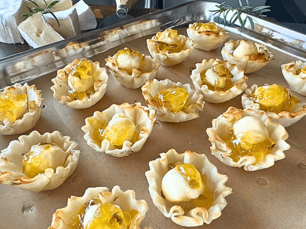 Close up photo of phyllo shells, brie cheese and peach pepper jelly on a wooden cutting board