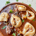 Close up photo of tortellini soup in a wooden bowl