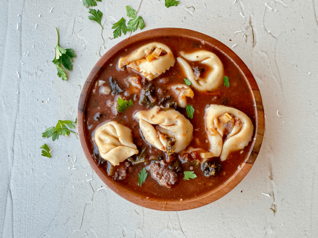 Close up photo of tortellini soup in a wooden bowl