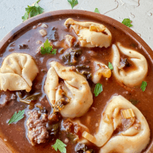 Close up photo of tortellini soup in a wooden bowl