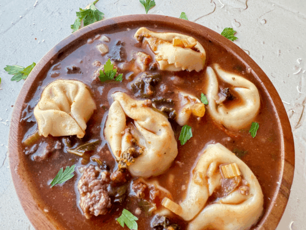 Close up photo of tortellini soup in a wooden bowl