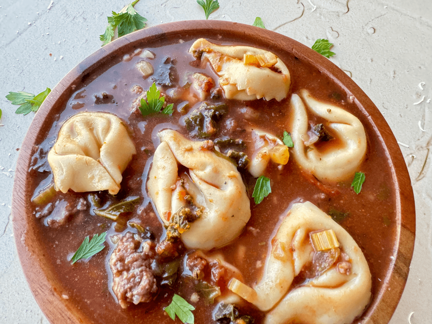 Close up photo of tortellini soup in a wooden bowl
