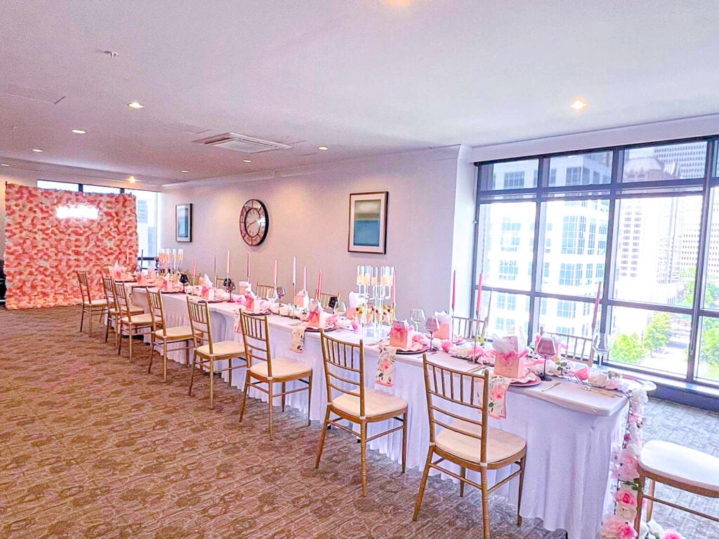 Photo of the room setup for the cuvée brunch party. There are white table cloths with pink flowers and candles on the table.