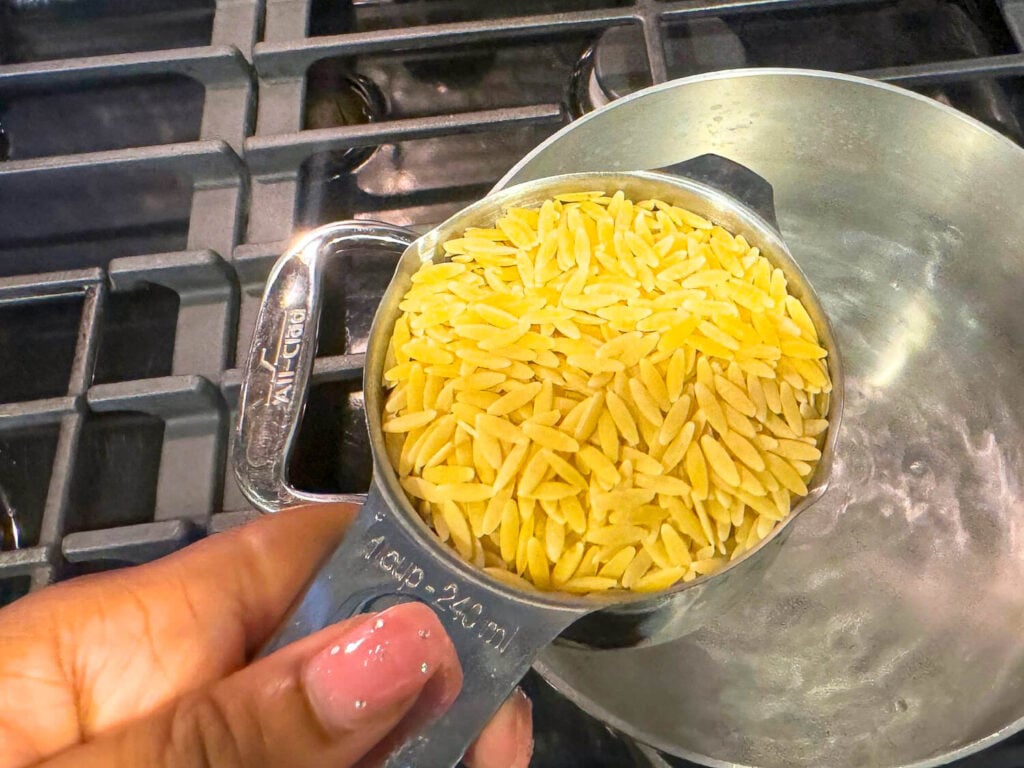 a photo of a cup of tried orzo pasta over a pot of boiling water