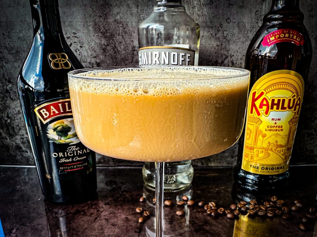 Photo of an espresso martini next to a bottle of Baileys, Vanilla Vodka , and Kahlua