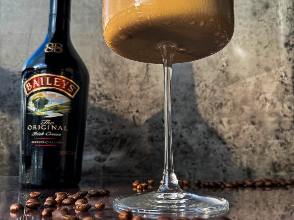Photo of an espresso martini next to a bottle of Baileys