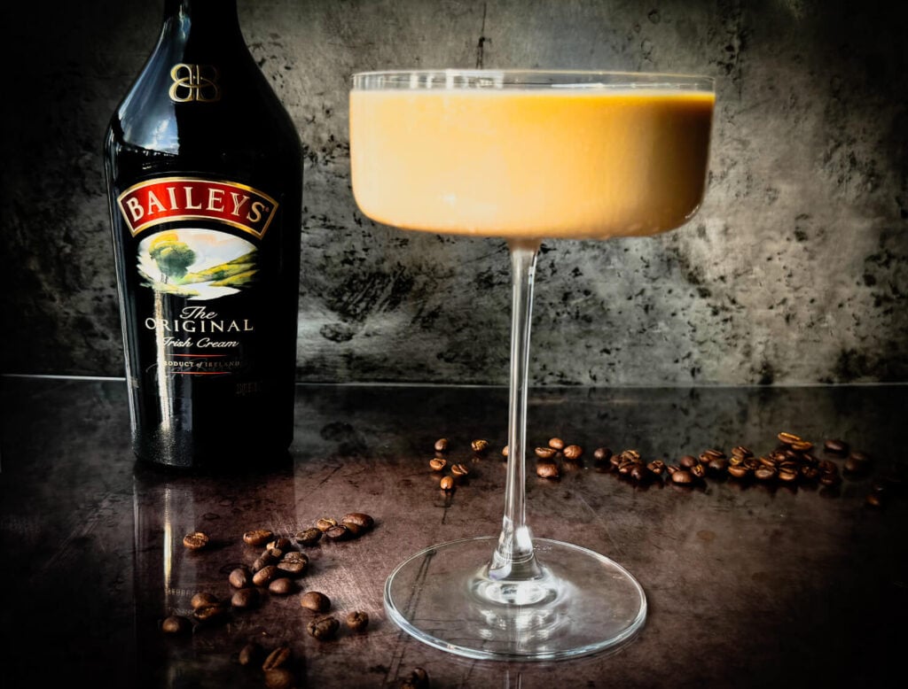 Photo of an espresso martini next to a bottle of Baileys