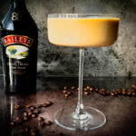 Photo of an espresso martini next to a bottle of Baileys