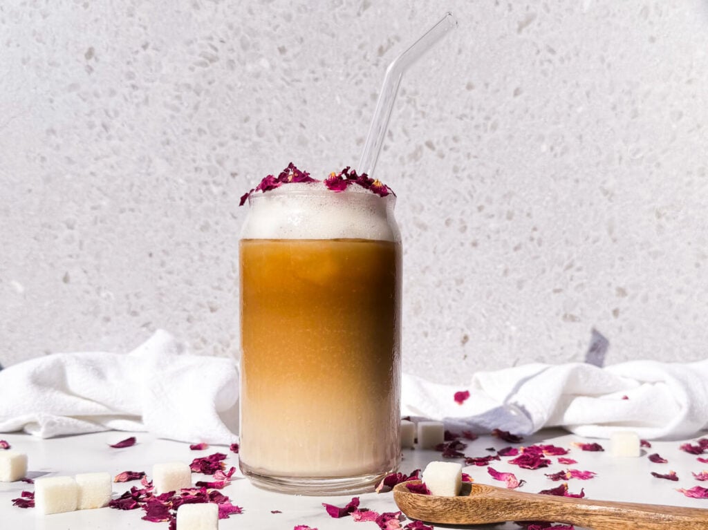 Photo of an iced rose latte in a glass cup surrounded by rose petals
