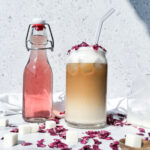 Photo of an iced rose latte next to a bottle of rose syrup