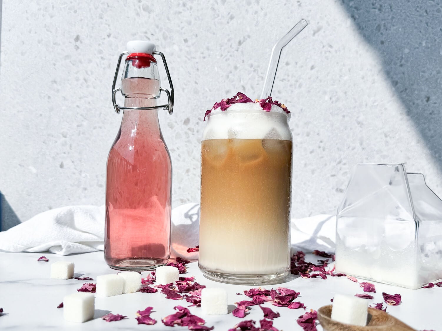 Photo of an iced rose latte next to a bottle of rose syrup
