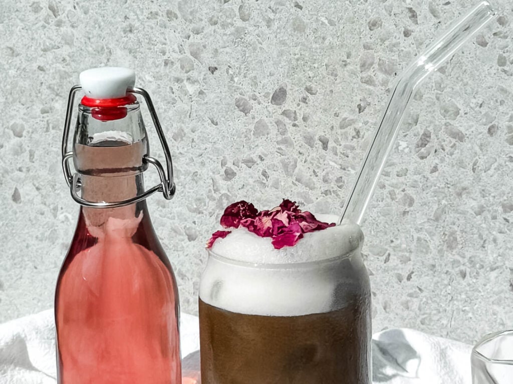 Photo of an iced rose latte next to a bottle of rose syrup
