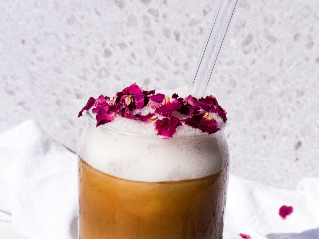 close up photo of Photo of an iced rose latte in a glass cup garnished with rose petals