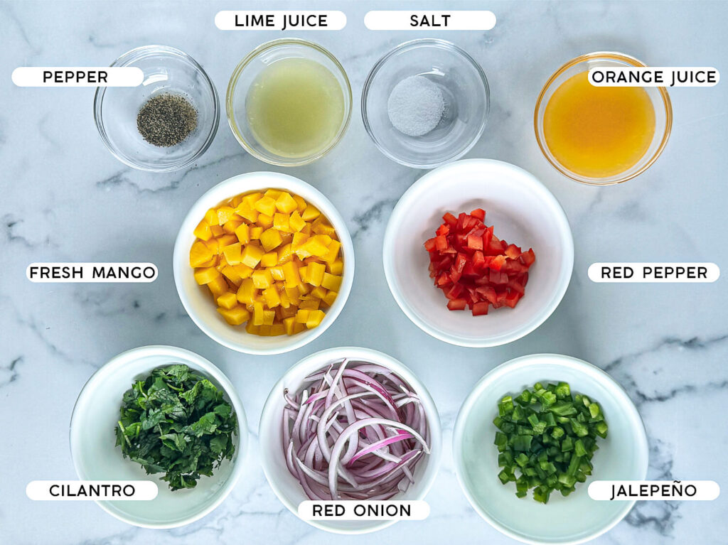 photo of mango salsa ingredients such as salt, pepper, lime juice, orange juice, diced mangos, red bell pepper, cilantro, red onions and jalapeño