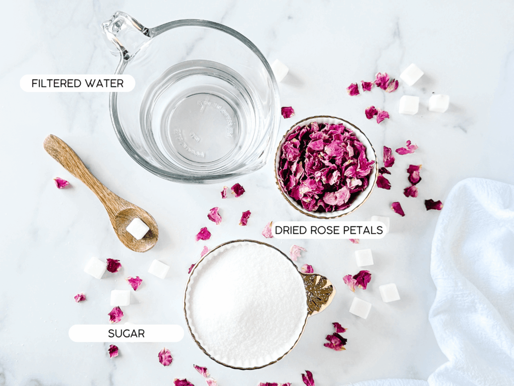 flat lay photo of ingredients needed. Filtered water, dried rose petals, and sugar