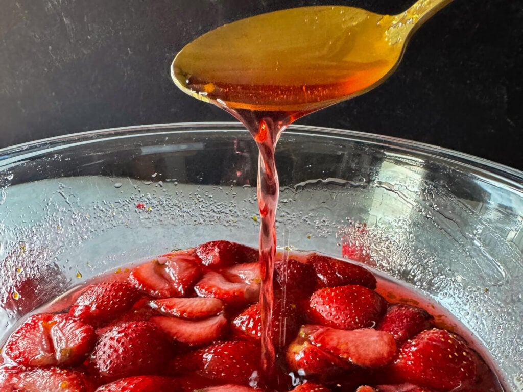 a photo of strawberry syrup pouring out of a gold spoon